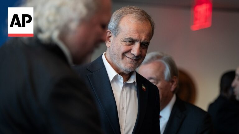 AP logo on the left; man in a dark suit smiles at a social event, other people in background.