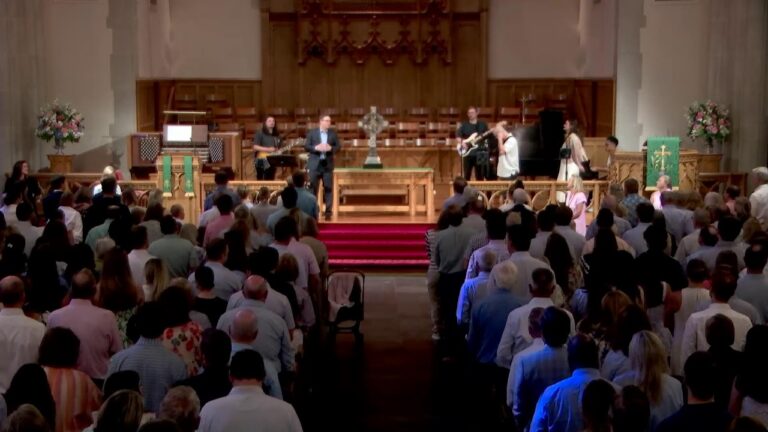 Church sanctuary with a worship band performing on stage while the congregation stands in the pews nearby.