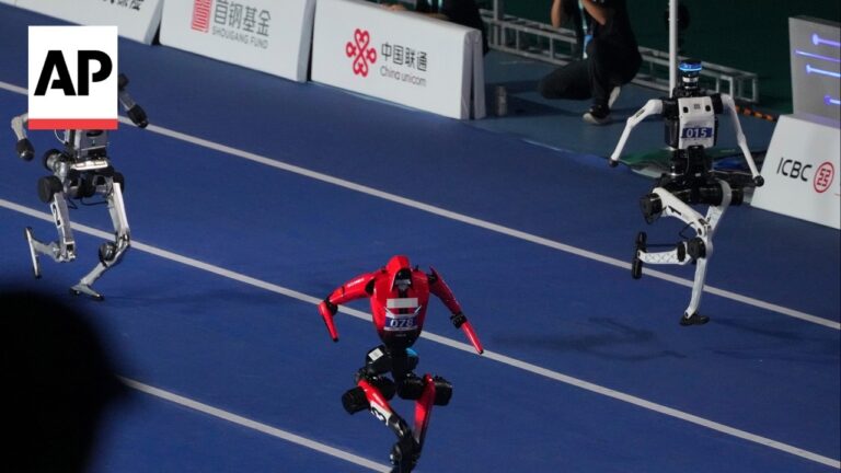 Red humanoid robot racing on a blue track, flanked by two white robots, AP logo visible in the corner.