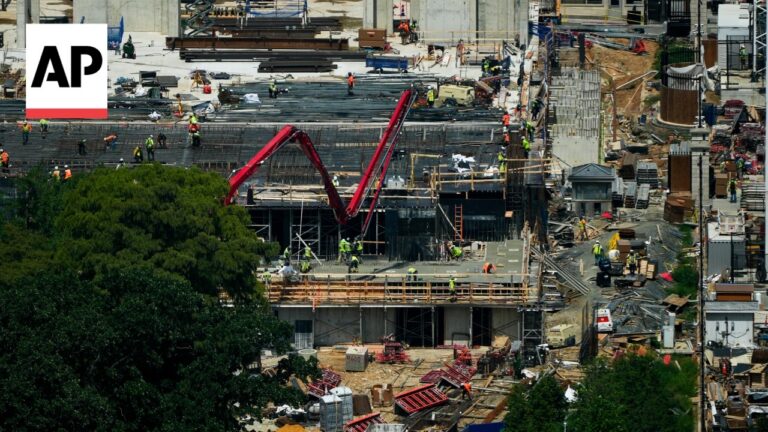 Construction site with workers, scaffolding, and heavy machinery; AP logo in the top-left corner.