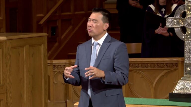 Man in a gray suit delivering a speech from a wooden pulpit inside a church.