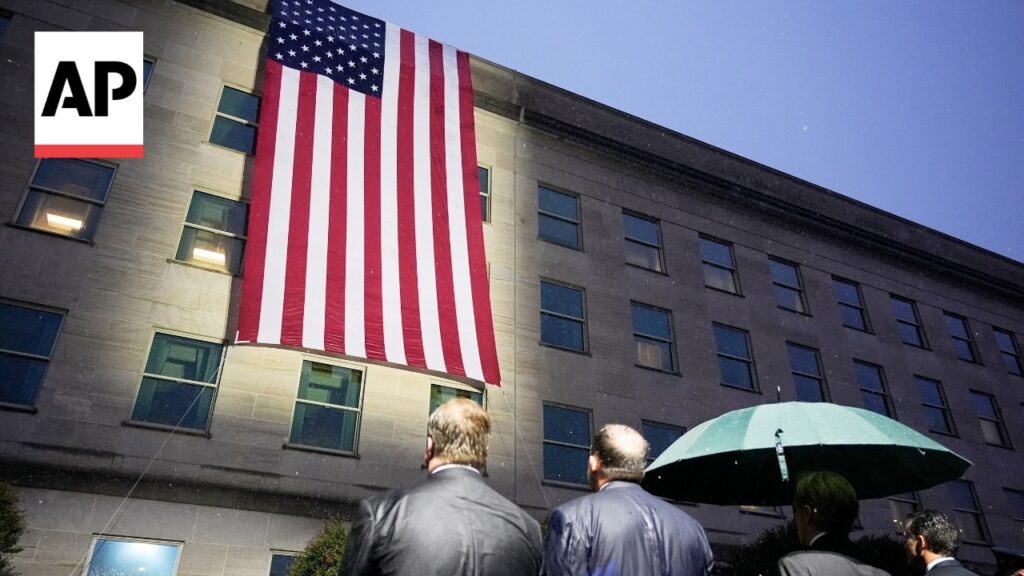 Large American flag draped down a gray stone building as three men in suits face it; AP logo in upper left.