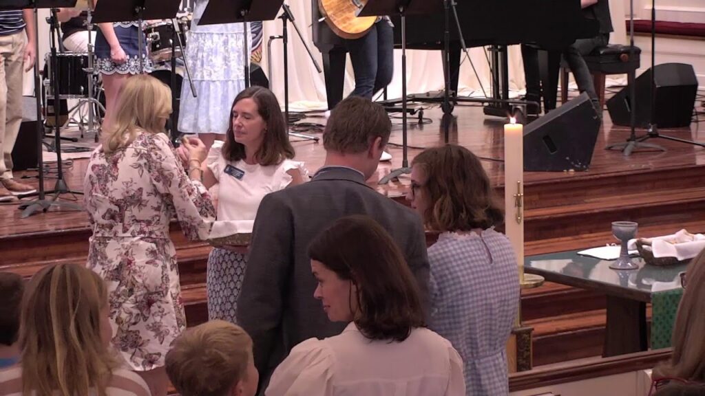 1789460717_maxresdefaultjpg - New Social Gospel People in semi-formal attire converse near a candlelit table on a church stage with musicians in the background.