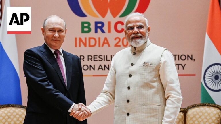Two world leaders shake hands at a BRICS event, with the Indian flag visible in the background and an AP logo on the left.