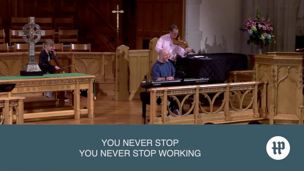 1789546470_maxresdefaultjpg - New Social Gospel Church musicians performing on a wooden stage: keyboardist singing into a mic with two violinists nearby, ornate woodwork and a cross in the background on stage.