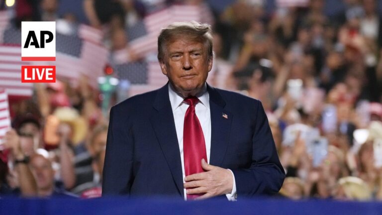 Man in a dark suit and red tie on a stage at a political rally, AP Live logo visible on the left.