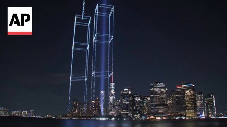Night view of a city skyline at night with blue wireframe outlines of two tall towers and an AP logo in the upper-left corner.