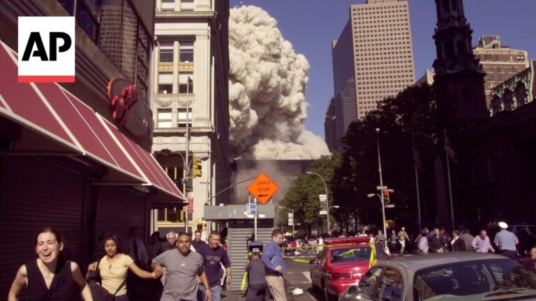 Crowded city street as people run away from a towering smoke plume rising behind a row of buildings; detour sign in foreground (AP logo top left).