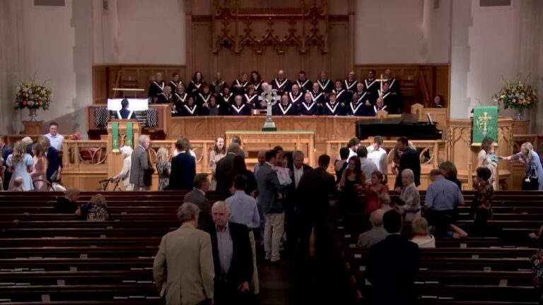 Church interior with a large choir onstage as attendees mingle in the nave before a service.