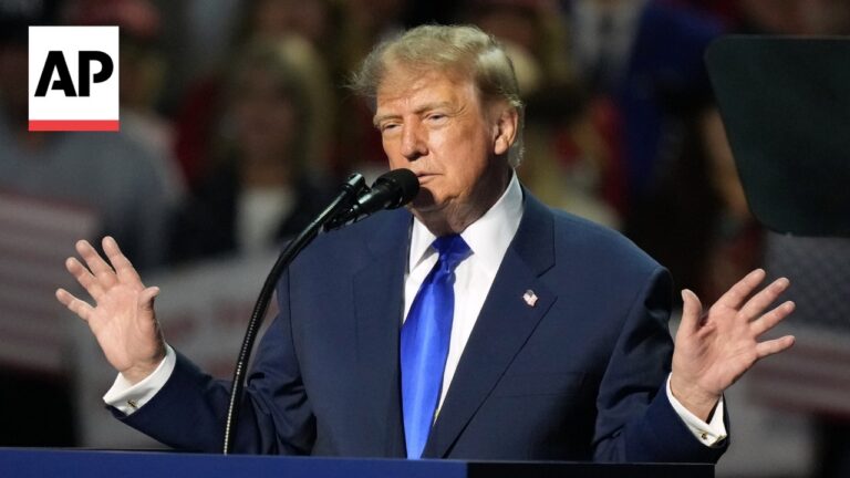Speaker at a podium with a microphone, wearing a dark suit and blue tie; AP logo in the corner.