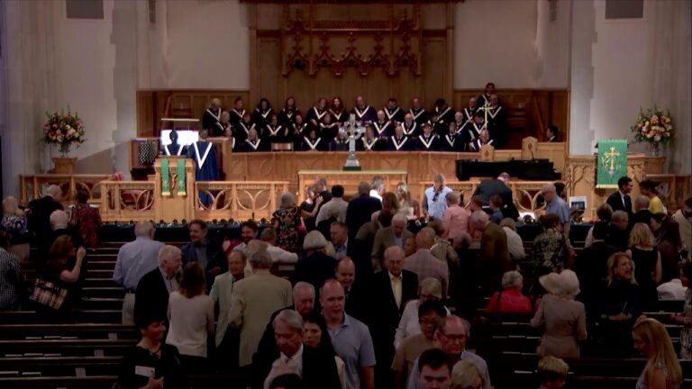 Church interior with a choir on the stage and attendees mingling in the pews behind them.