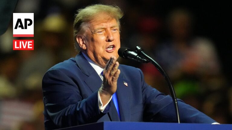 Man in a blue suit delivering a speech at a podium, microphone nearby, AP Live logo on the left.