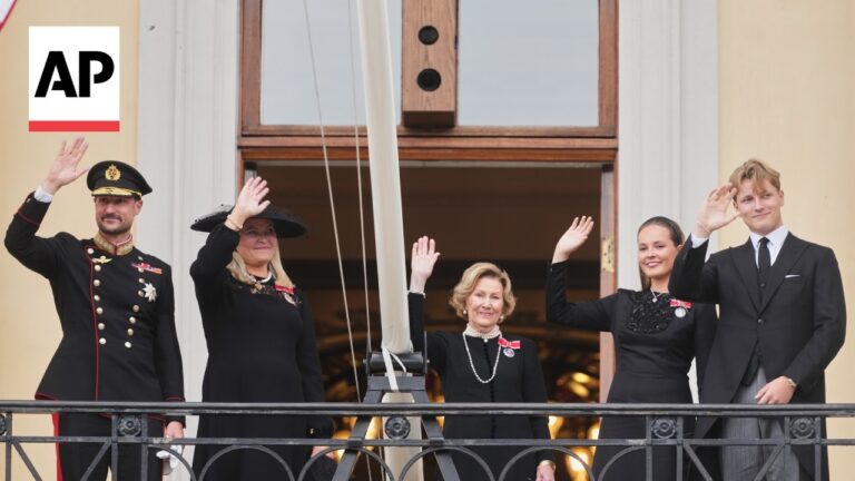 Five formally dressed dignitaries wave from a balcony, including a uniformed man on the left and others in black outfits, with an AP logo in the corner.]','Five people stand on a balcony, waving to a crowd; military officer, women in black dresses, and a man in a suit.'],