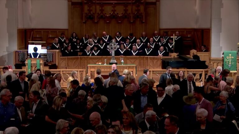 Chancel of a church with a choir on the balcony behind the altar and a crowd mingling in the nave
