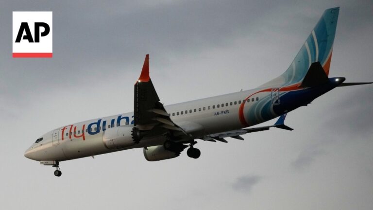 Flydubai passenger jet in descent with landing gear down against a cloudy sky, AP logo in the corner.