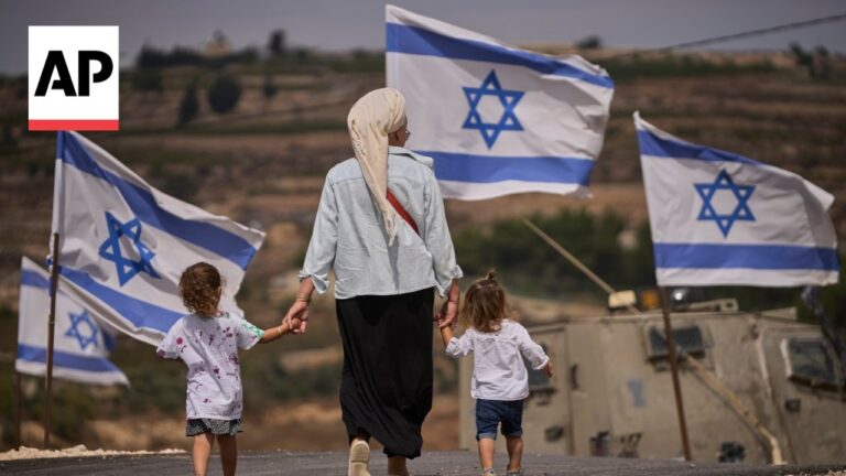 Woman walking with two children, holding hands, alongside Israeli flags and a military vehicle in a desert landscape; AP news image stamp visible.
