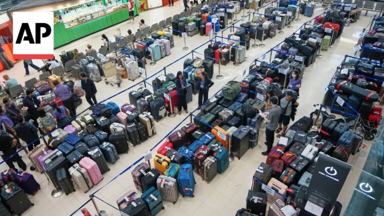 Busy airport baggage area with rows of suitcases behind blue rope barriers as travelers browse and staff assist; AP logo visible in the top-left corner.