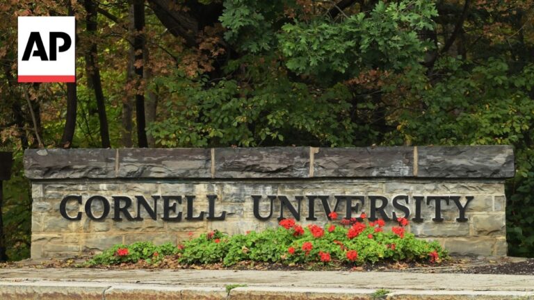 Cornell University stone sign with red flowers in front and greenery in the background; AP news logo top-left corner.