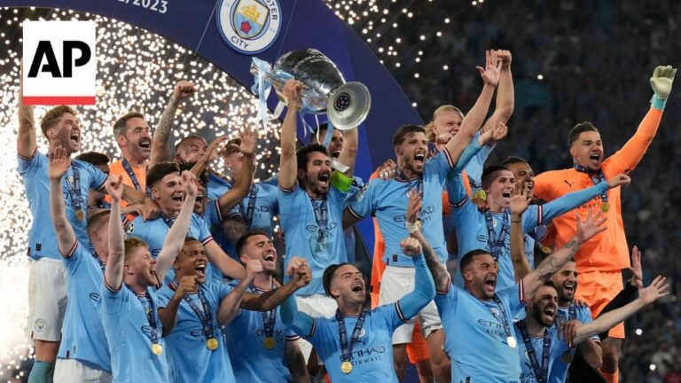 Manchester City players celebrate a victory, lifting the trophy with gold medals as confetti rains down on them.