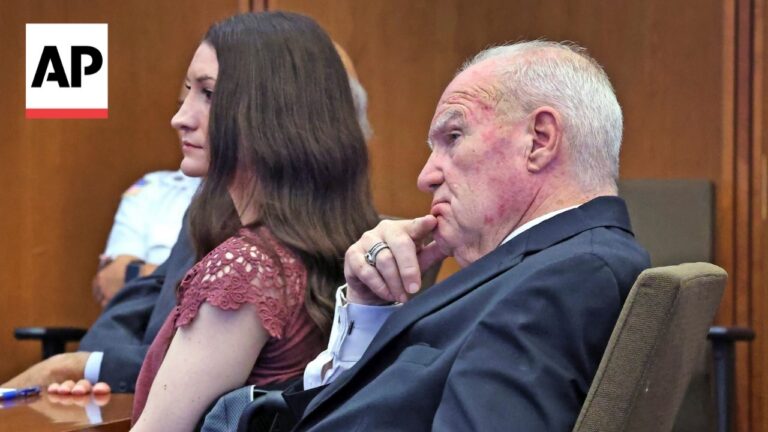 AP News photograph of a man in a suit with bruises on his face sitting in a courtroom, his hand on his chin, beside a young woman with brown hair in a maroon lace dress