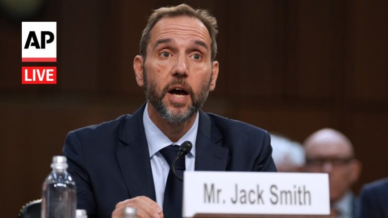 Man in a navy suit testifying at a formal hearing, speaking into a microphone with a water bottle nearby; nameplate reads 'Mr. Jack Smith' and AP Live logo appears left.