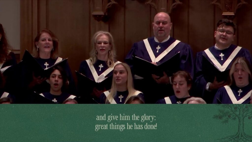 1792433412_maxresdefaultjpg - New Social Gospel Church choir performing on stage in purple robes with cross insignia, green banner with verse in front.