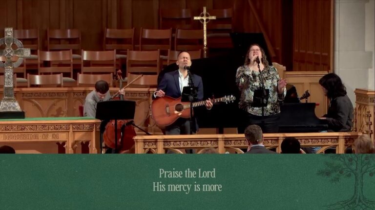 Worship band on a church stage: guitarist and vocalist at microphones, a pianist, and a cellist behind them.