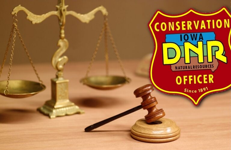 Brass scales of justice and a wooden gavel on a desk, with an Iowa DNR Conservation Officer badge in the top-right corner.