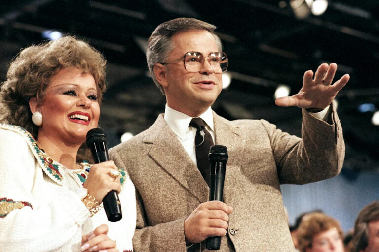 Smiling woman and man on stage holding wireless microphones, addressing an audience during a live event.