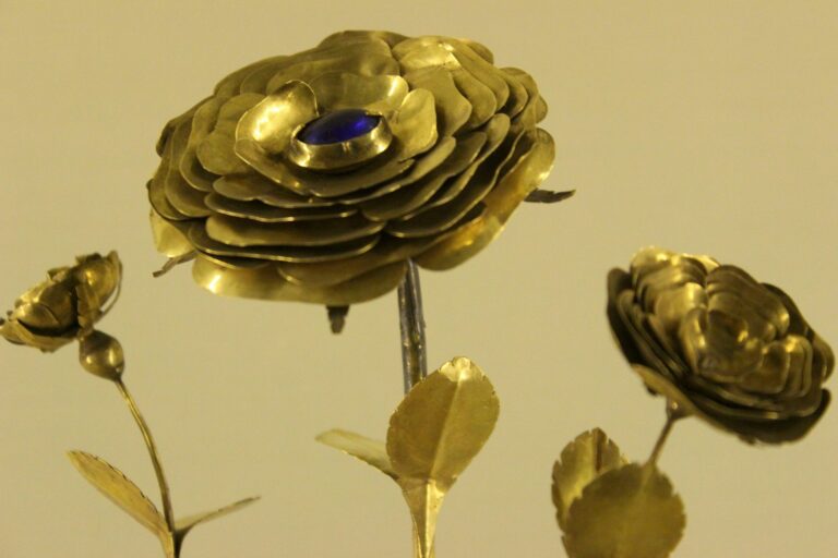 Gold metallic rose sculpture with layered petals and a blue gem at the center