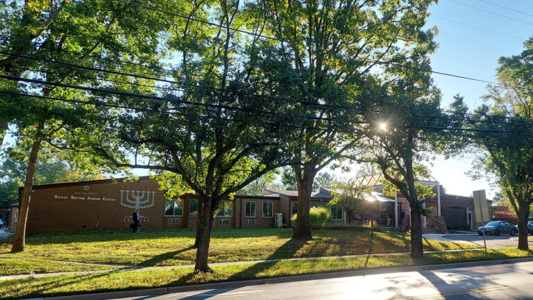 Brick synagogue building labeled Silver Spring Jewish Center, seen from the sidewalk with trees and overhead power lines.