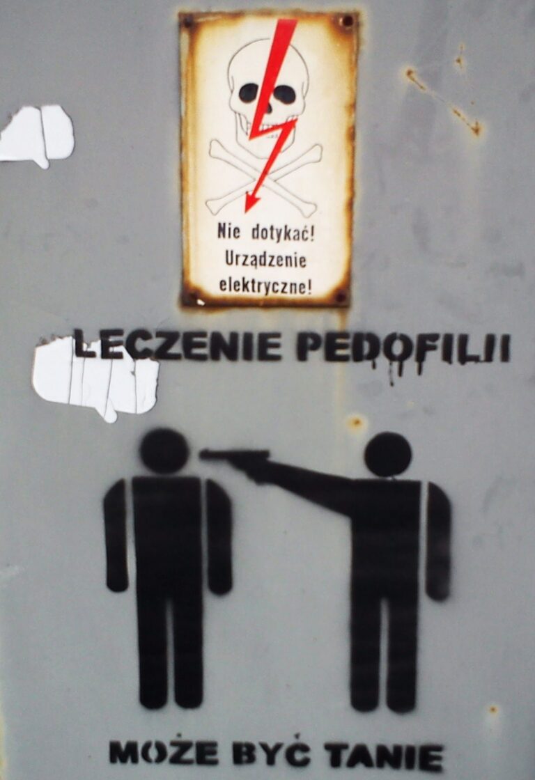Sign: 'Nie dotykać! Urządzenie elektryczne!' with skull and crossed bones and a red lightning bolt — warning not to touch electrical equipment.