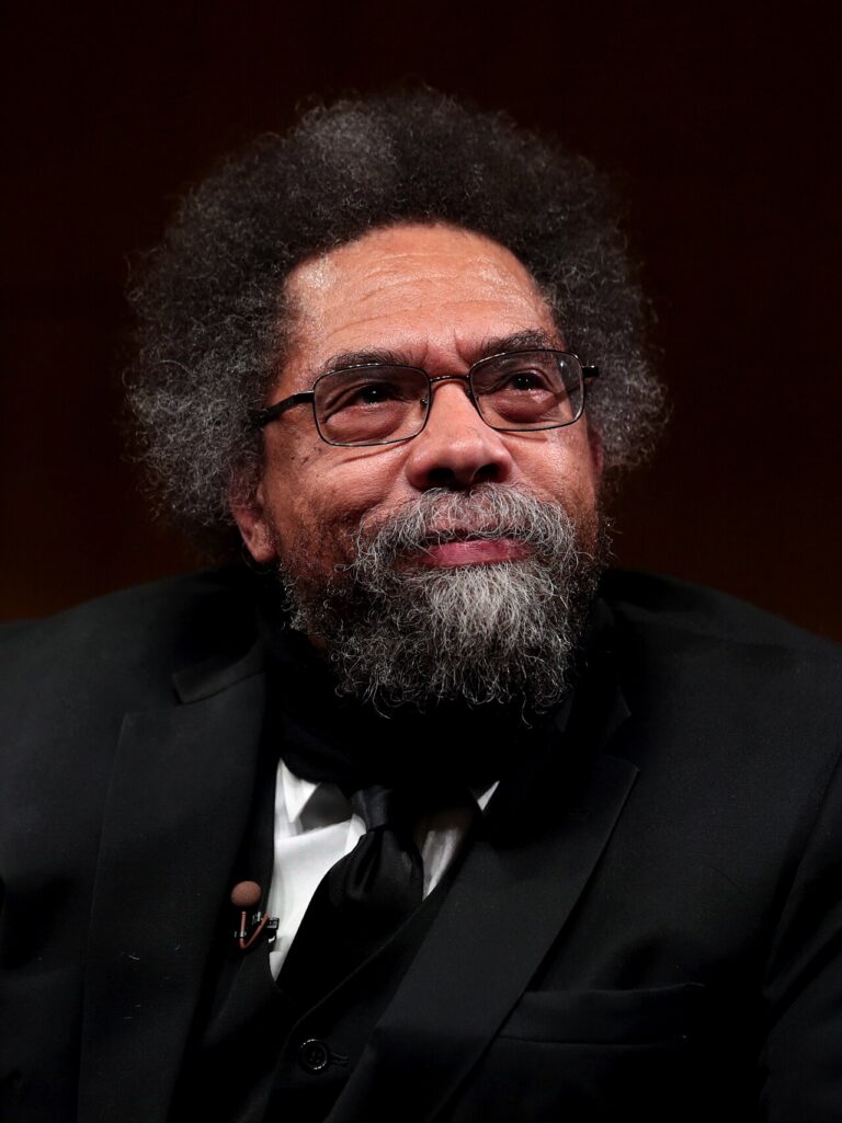 Close-up of a bearded man with glasses wearing a black tuxedo, looking thoughtful.
