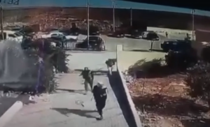 Security camera footage of two people running along a sidewalk beside a parking lot.